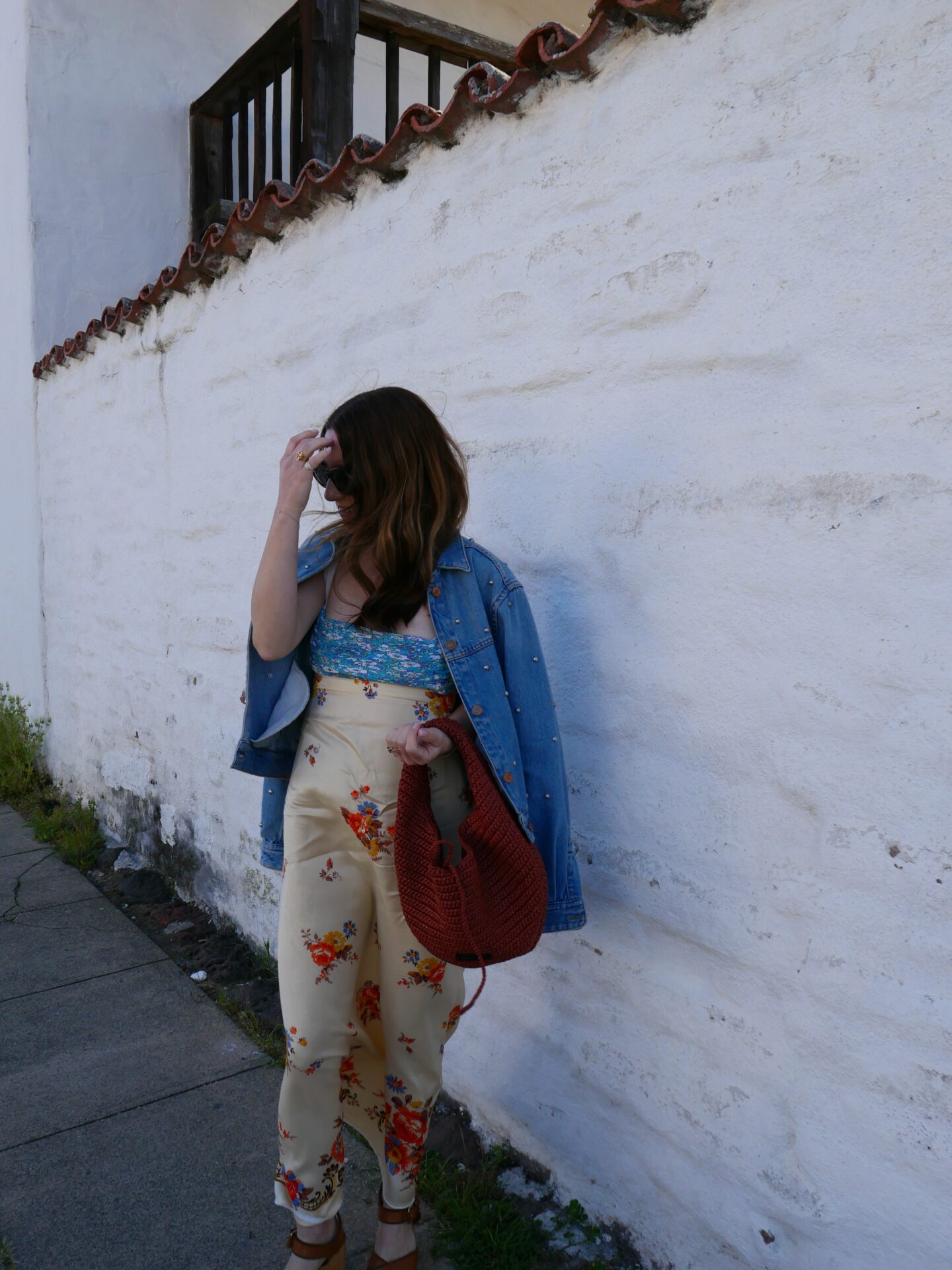 woman standing near a wall and wearing denim jacket, dress with floral prints and holding a red bag in Sonoma