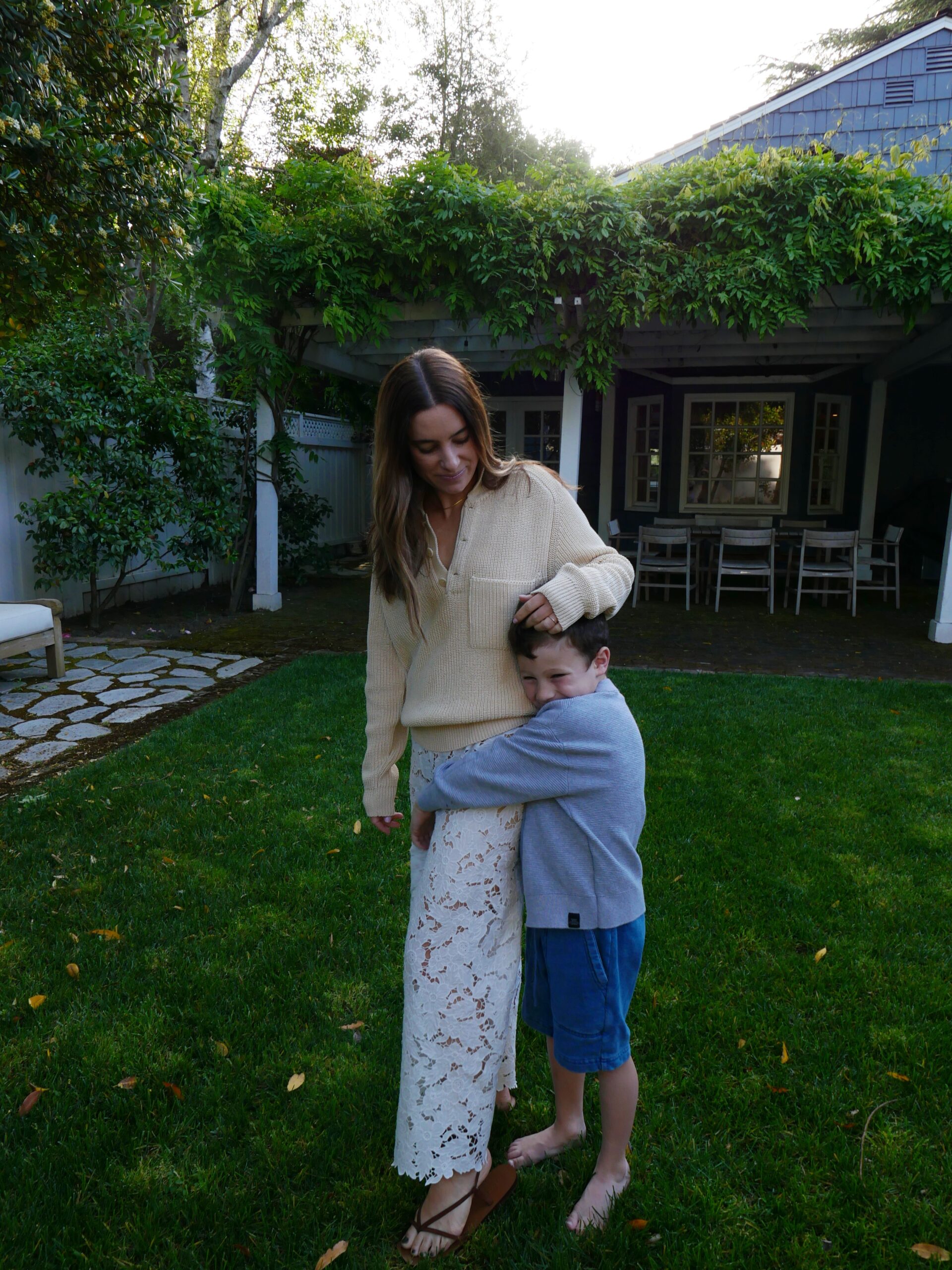 woman in Shaina Mote sweater and lace dress with her son hugging her