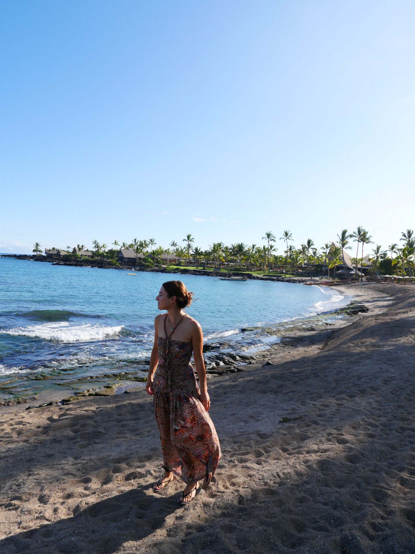 Alicia Lund wearing a maxi dress and standing at the shore of Kona Village